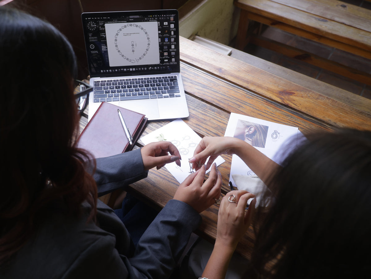 Two people sitting at a wooden table with a laptop and books, engaged in an activity.